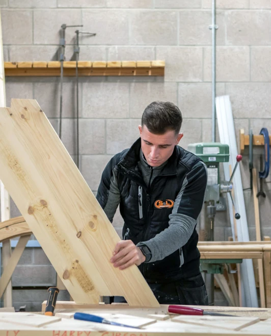 A joinery student carefully positioning a large wooden panel in preparation for assembly in a woodworking workshop. A joinery student carefully positioning a large wooden panel in preparation for assembly in a woodworking workshop.